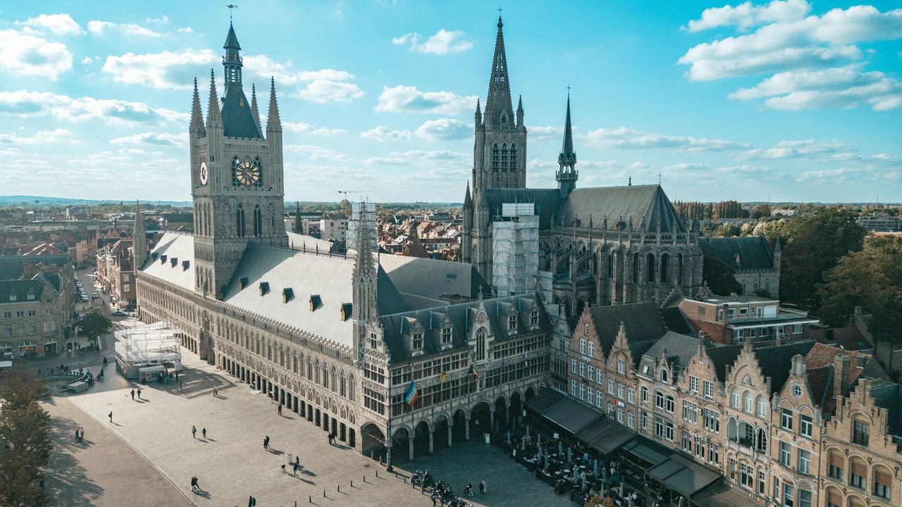 Vue sur la Grand-Place d'Ypres avec les Halles aux draps reconstituées et la Porte de Menin en arrière-plan au crépuscule