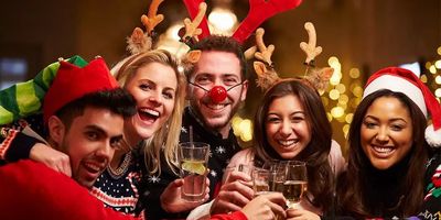 A joyful group of five friends smiling and clinking glasses together at a Christmas party, wearing festive attire like reindeer antlers, a Santa hat, an elf hat, and holiday sweaters.