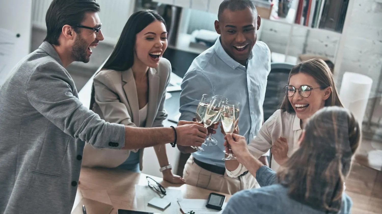 Bovenaanzicht van een diverse groep van vijf glimlachende collega's die klinken met champagnefluiten om een succes te vieren in hun kantoor.