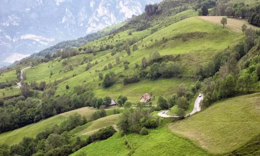 Un paysage rural de montagne en France avec une petite maison et une route sinueuse entourée de verdure