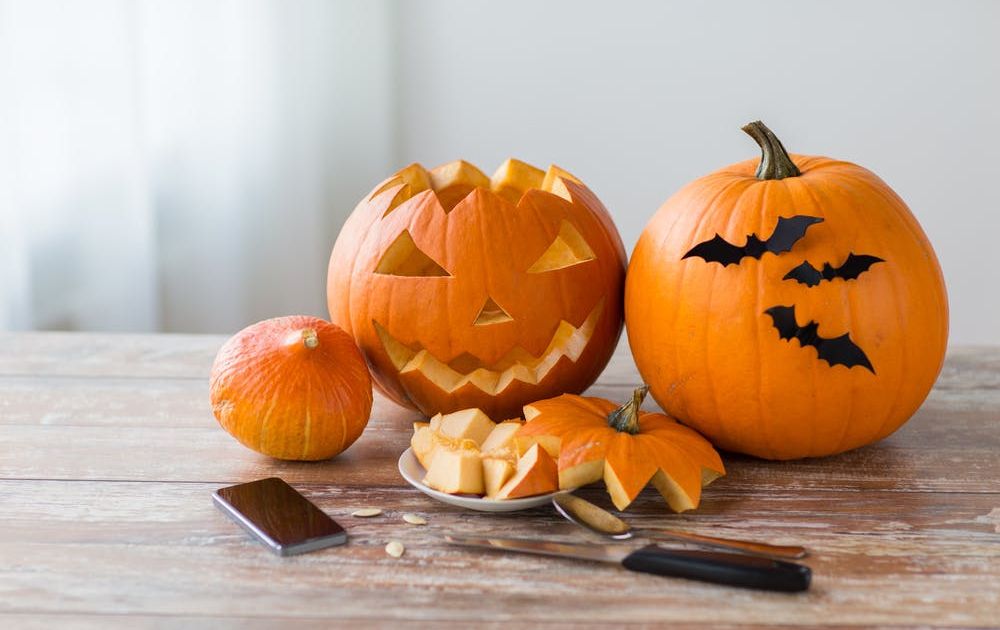 A close-up of a wooden table filled with Halloween decorations, popcorn in a spiderweb bowl, and small pumpkin buckets, with people in costumes sitting blurred in the background.