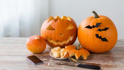 A close-up of a wooden table filled with Halloween decorations, popcorn in a spiderweb bowl, and small pumpkin buckets, with people in costumes sitting blurred in the background.