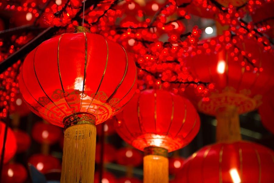 A close-up shot of glowing red Chinese lanterns with gold tassels hanging amidst red blossom decorations, commonly used for Chinese New Year.